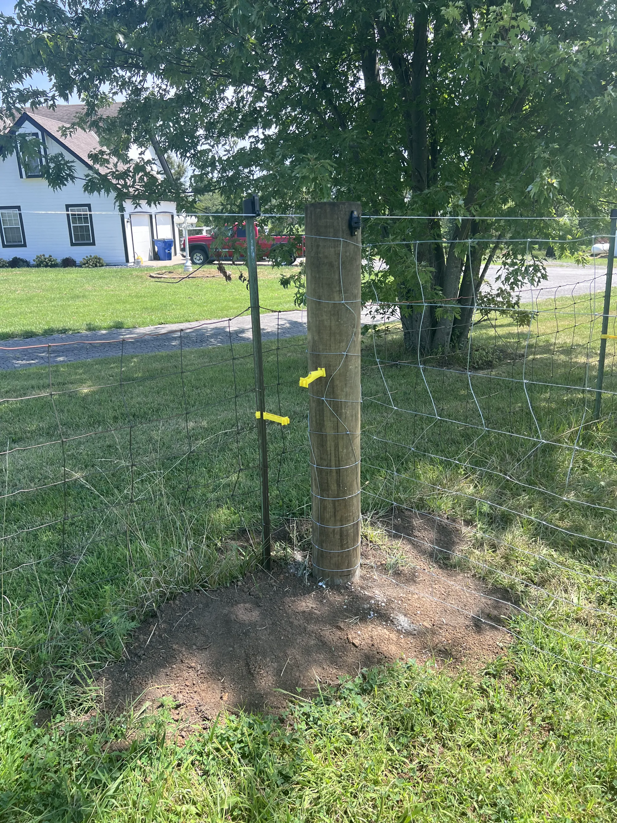 Close view of electric fence wire, mesh, and yellow gate handles around a wooden post
