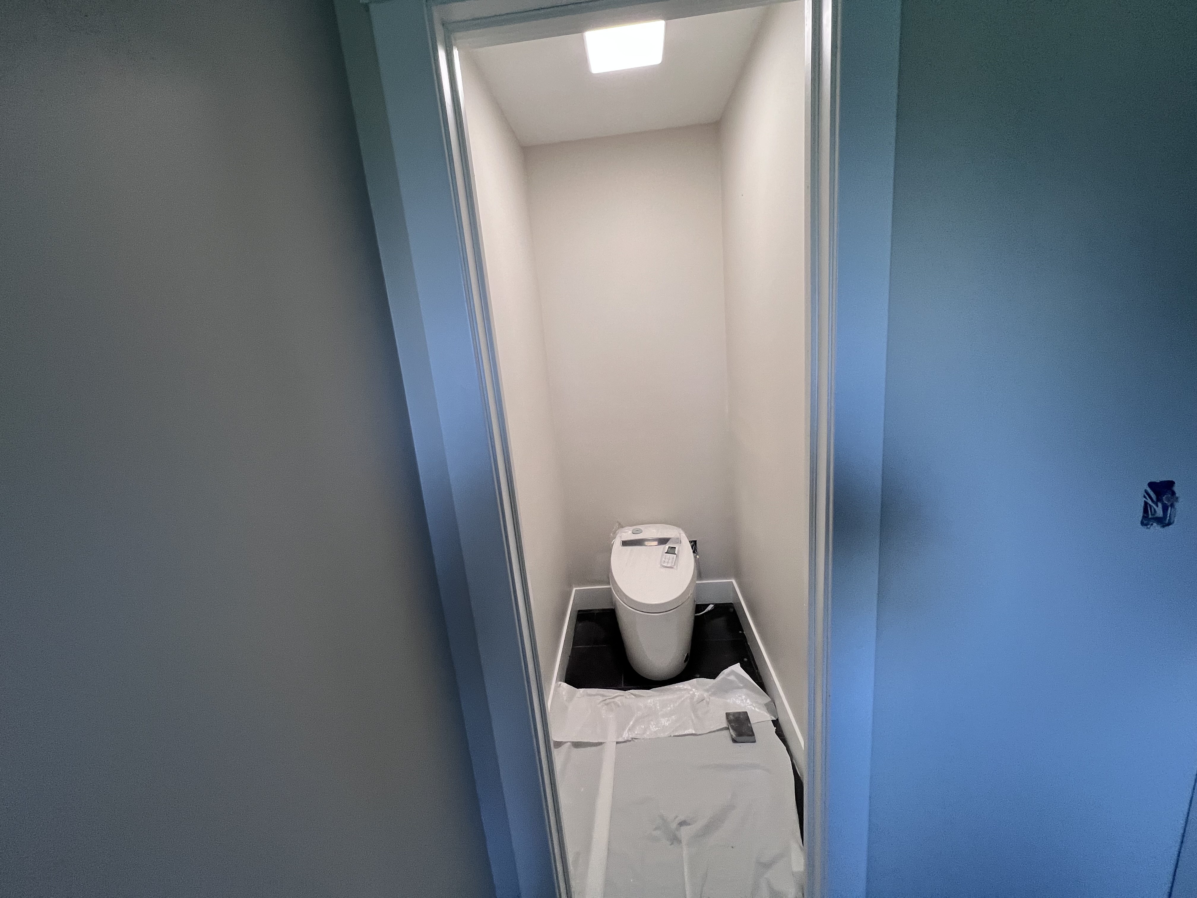 The main suite toilet room with a modern toilet on dark tile floor, painted gray walls, and a drop cloth still in place