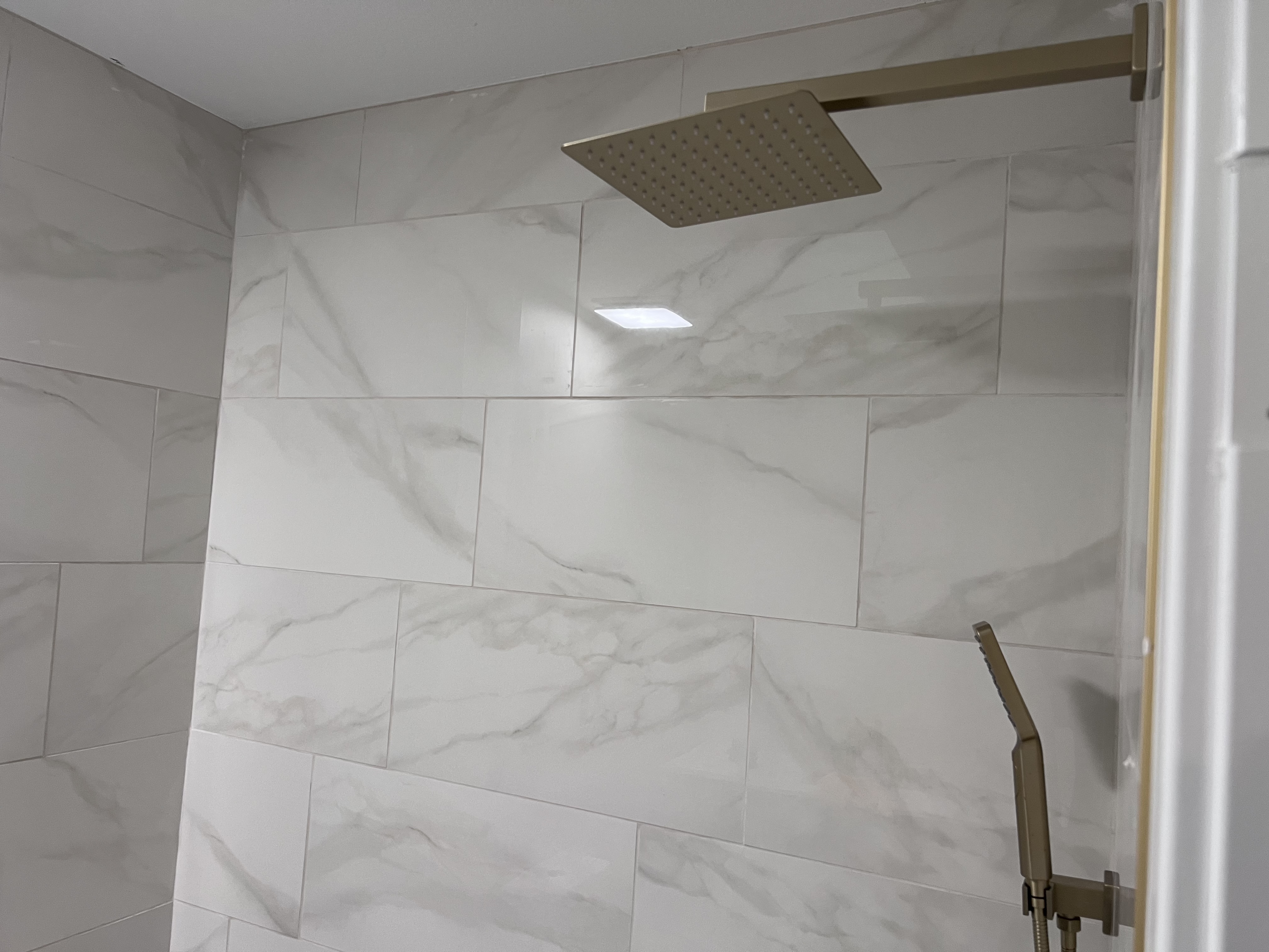 A close-up of marble-pattern tile shower wall with a square gold rainhead above