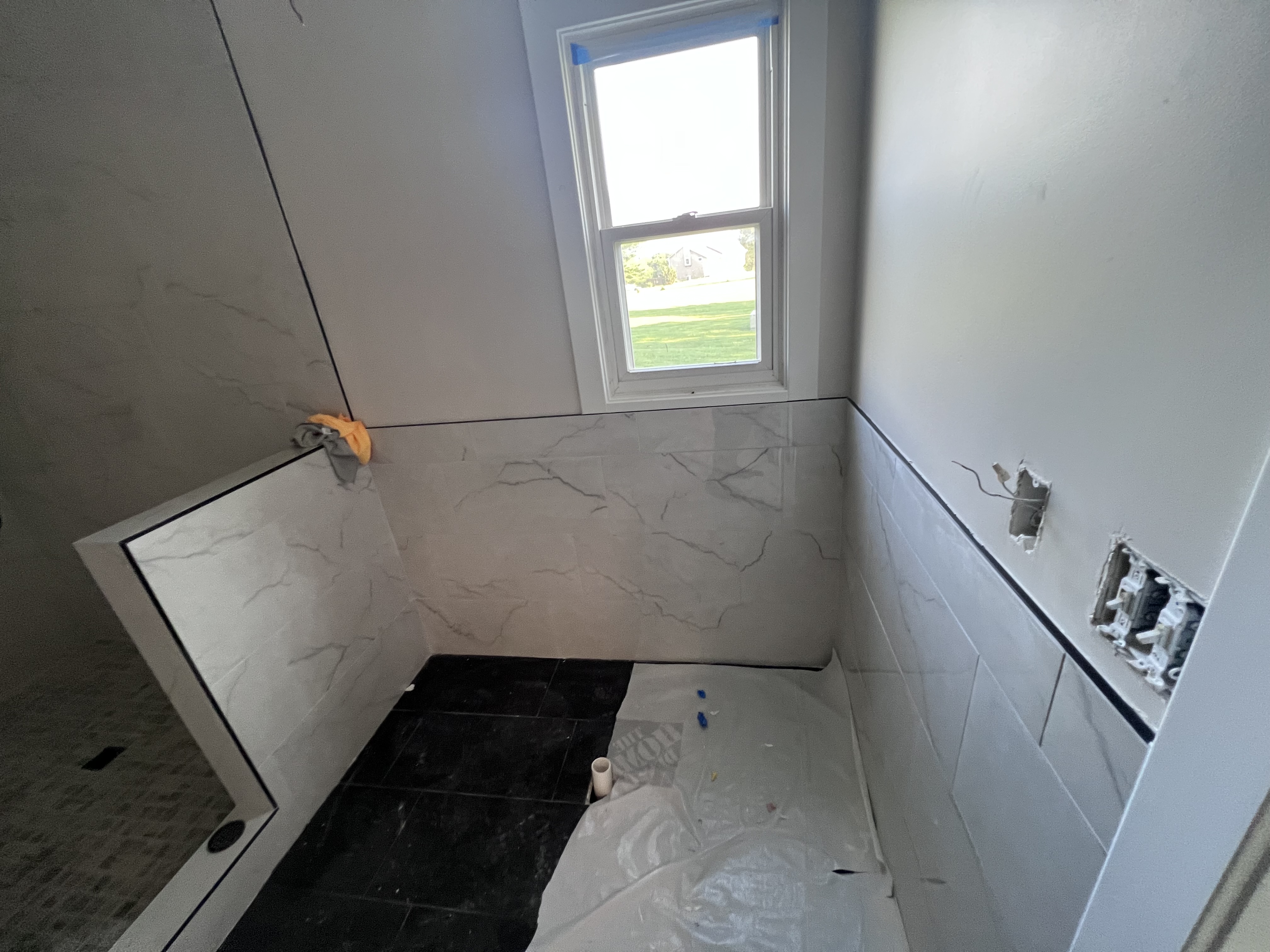 A tiled shower stall with marble-look tile on the walls, dark tile floor, and a window with a view of the yard